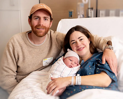 A young couple holding a newborn in a hospital bed after just giving birth to the first baby of 2025