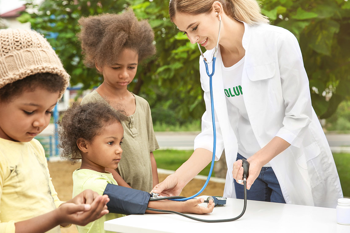 Nurse standing with three young girls and measuring their blood pressure.